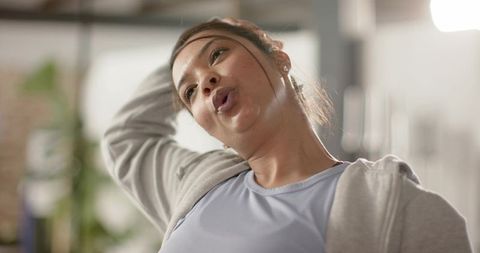 Asian woman stretching neck during gym warm-up wearing hoodie and light-blue athletic top