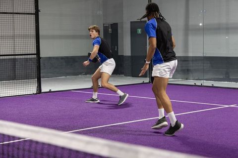 Dynamic doubles padel players reacting to incoming ball on vibrant purple court