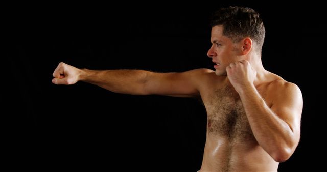 Male athlete practicing punching technique against a dark background, showing intense focus and fitness. Ideal for use in articles and materials related to martial arts training, combat sports, fitness, and physical endurance regimes.