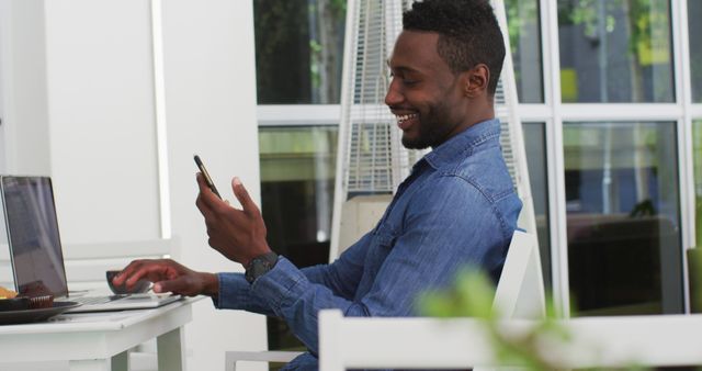 Man smiling while using smartphone and laptop indoors - Download Free Stock Images Pikwizard.com