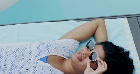 Indian woman relaxing poolside wearing white lace coverup and lifting round sunglasses