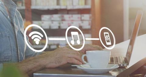 Typing on laptop in sunlit cafe with coffee cup and wireless music streaming icons