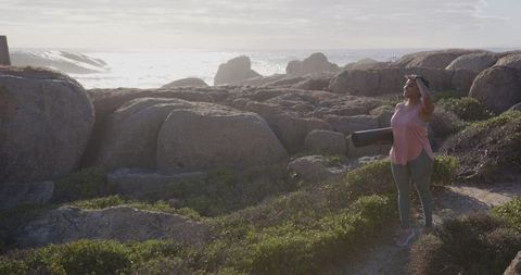 Asian indian woman with yoga mat on scenic coastal trail at sunset
