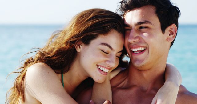 A young Caucasian couple shares a joyful embrace by the sea, with copy space. Their laughter and closeness convey a sense of happiness and romantic connection.