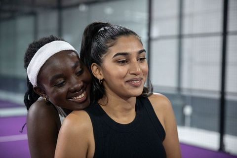 Multicultural women embracing playful moment on indoor padel court after workout