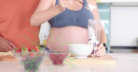 Pregnant woman preparing breakfast smoothie with yogurt and berries in modern kitchen