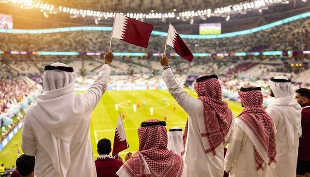 Cheering qatari fans waving national flags at nighttime football match in modern stadium