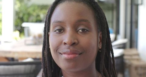 Relaxed african woman with dreadlocks and jewelry smiling on sunlit veranda close-up