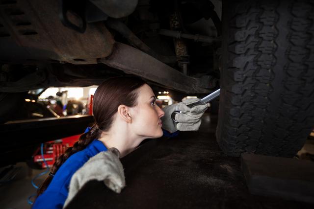 Female mechanic inspecting car tire in repair garage. She is using a flashlight to closely examine the tire's condition. Ideal for illustrating automotive services, gender diversity in technical professions, and professional car maintenance. Suitable for use in advertisements, articles, and websites related to car repair, mechanic training, and automotive industry.