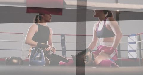 Female boxers adjusting hand wraps and gloves kneeling in boxing ring before sparring