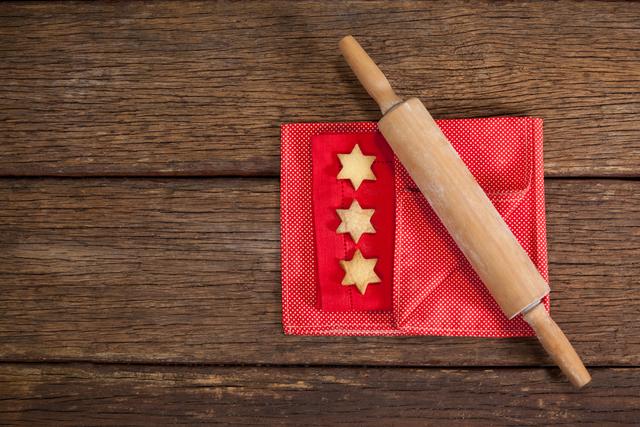 Perfect for holiday-themed content, this image showcases star-shaped Christmas cookies and a rolling pin on a rustic wooden table. Ideal for use in baking blogs, holiday recipe websites, festive greeting cards, and social media posts celebrating the joy of homemade holiday treats.