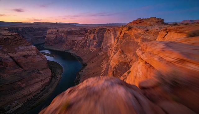 Dramatic sunset canyon overlooking meandering river from red rock ledge