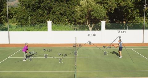 Senior pair playing tennis on outdoor court under sun