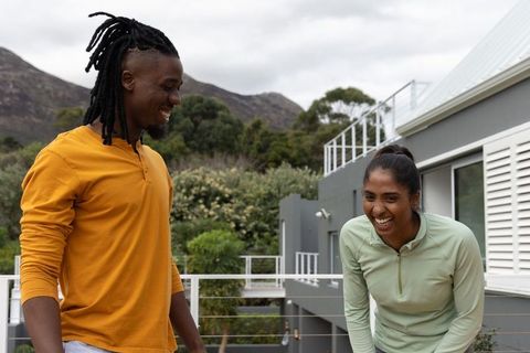 Laughing couple sharing relaxed balcony moment on modern terrace with mountain backdrop