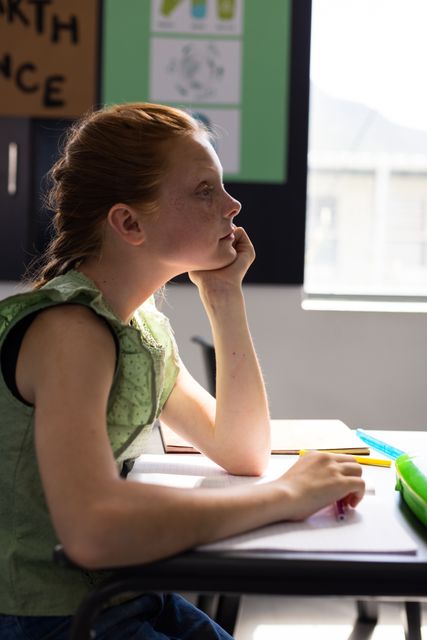 Caucasian schoolgirl sitting at desk, attentively listening to teacher in elementary school classroom. Ideal for educational materials, school brochures, academic websites, and articles about childhood learning and education.