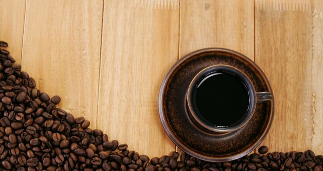 A cup of black coffee sits on a saucer surrounded by coffee beans on a wooden surface, with copy space. Coffee enthusiasts often appreciate the visual appeal of freshly brewed coffee alongside the raw beans it came from.