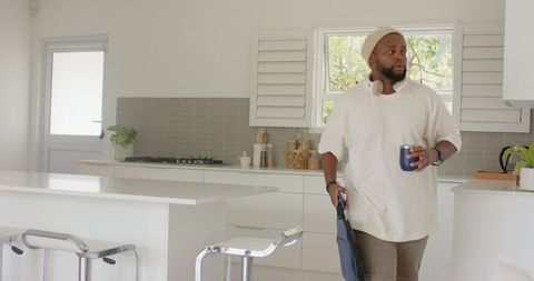 African american man standing holding mug and folded umbrella in minimalist modern kitchen