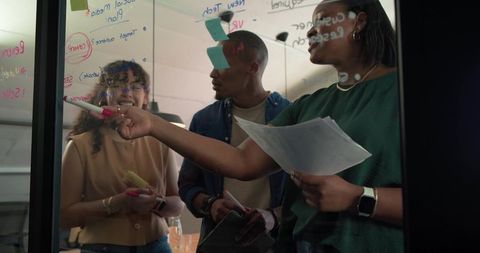 Diverse team brainstorming on glass whiteboard collaborating on creative project planning