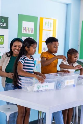 Children sorting paper and plastic recycling in classroom with teacher guiding activity