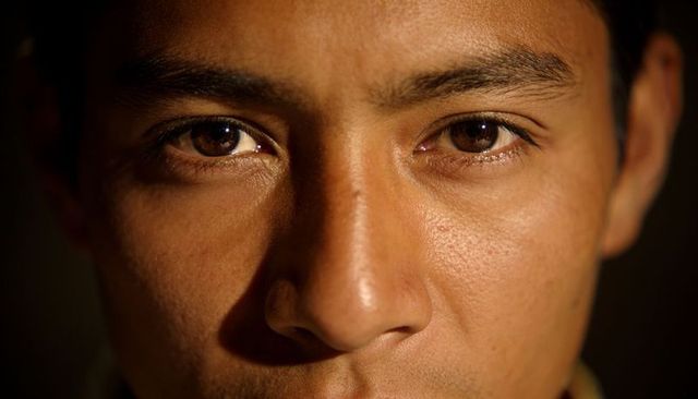 Close-up portrait young man with brown eyes and textured skin in dramatic low light