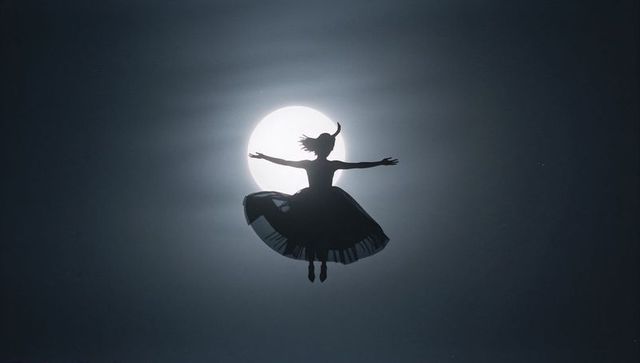 Dancer's silhouette leaping gracefully against full moonlit sky