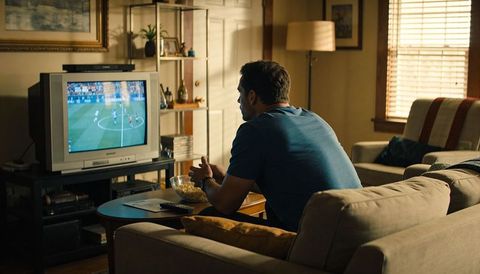 Man watching soccer on vintage crt tv from couch eating popcorn and holding remote