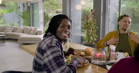 Black man smiling at breakfast gathering with friends around wooden dining table in modern home