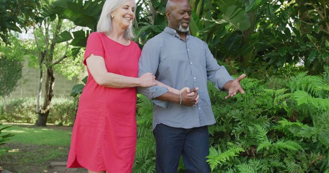 Happy senior diverse couple walking in garden. Spending quality time at home and retirement concept.
