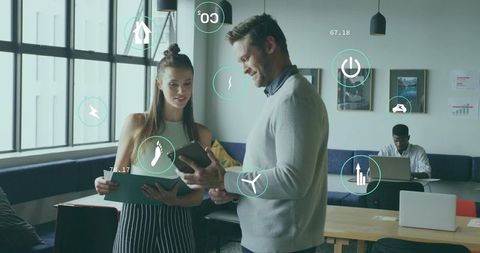 Colleagues Reviewing Data on Tablet with Informative Icons in Modern Office