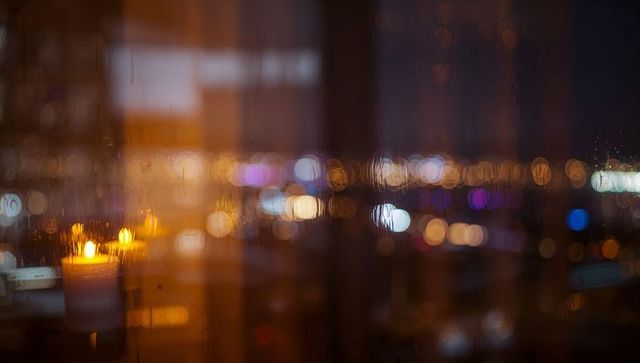 Flickering candle glowing through rain-streaked window with city bokeh night atmosphere