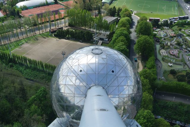 Photo features an aerial view of Atomium, an iconic landmark in Brussels, Belgium, surrounded by sports fields and lush greenery. Ideal for use in articles or projects about travel, architecture, famous landmarks, and recreational spaces. Perfect for content related to tourism, sightseeing, cultural heritage, or showcasing the cityscape and outdoor activities in Brussels.