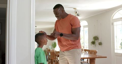 African american father measuring son height tracking growth, smiling, bonding at home