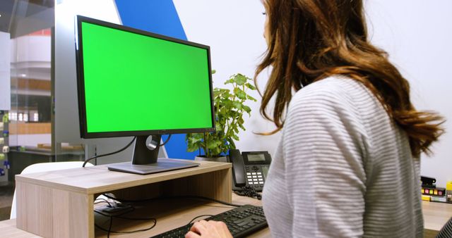 This depicts a woman working at a computer with a green screen at a desk in a modern office. Ideal for use in business, technology, remote work, and professional workplace illustrations.
