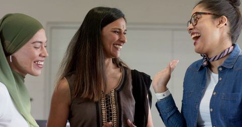 Diverse female colleagues laughing and bonding in bright minimalist office meeting room