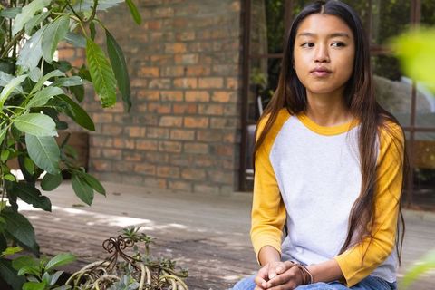 Contemplative Teenage Girl Sits on Wooden Terrace with Plants