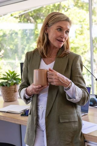 Woman in Office Holding Coffee Mug and Speaking by Desk