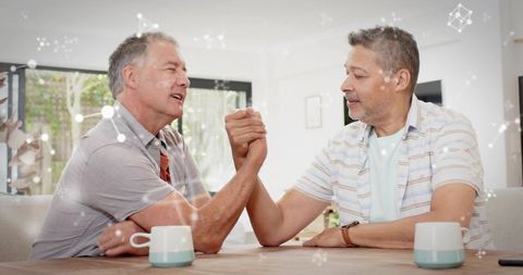 Two mature men arm-wrestling at home showing friendly competition and strong camaraderie