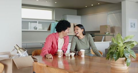 Diverse Couple Laughing with Coffee Amid Moving Boxes