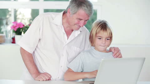 Grandfather Assisting Grandchild with Laptop in Modern Kitchen