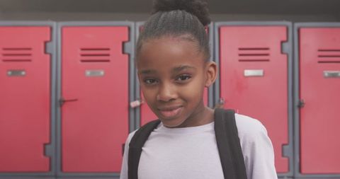 Confident schoolgirl standing by school lockers
