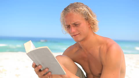 Blonde Man Engrossed in Book on Ocean Beach
