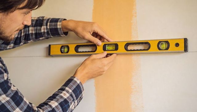 Handyman holding yellow spirit level leveling drywall for interior renovation and precise measuring