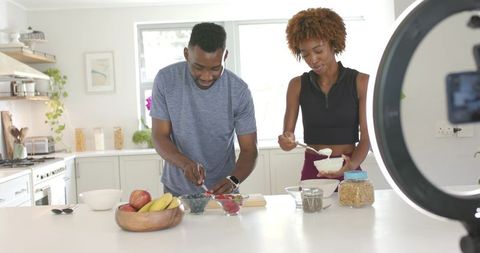 Diverse couple preparing healthy yogurt bowls at home kitchen island with ring light