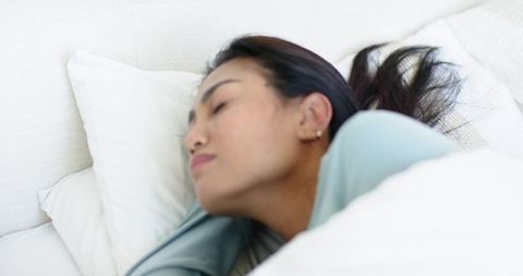 Asian woman resting peacefully on white bed sleeping in cozy minimalist bedroom serene morning