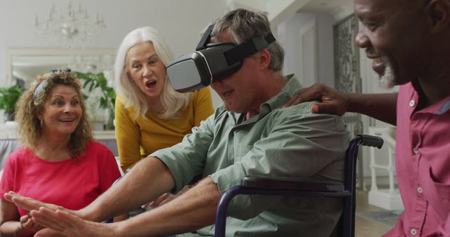 Image of happy senior man in wheelchair using vr headset and having fun with diverse friends. retirement lifestyle, disability, spending quality time with friends and technology.