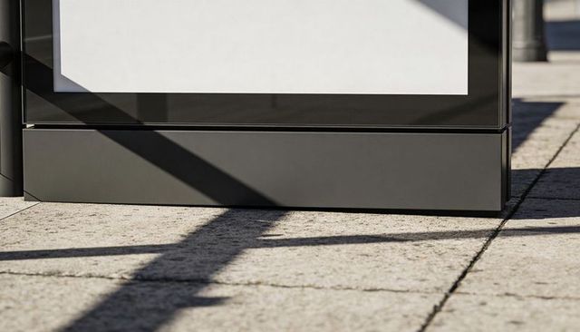 Blank urban advertising panel with dark metal base and diagonal shadows on concrete plaza