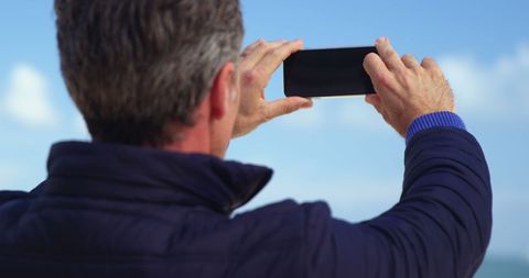 Man capturing landscape with smartphone under clear sky