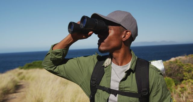 African american man hiking by the coast using binoculars. fitness training and healthy outdoor lifestyle.