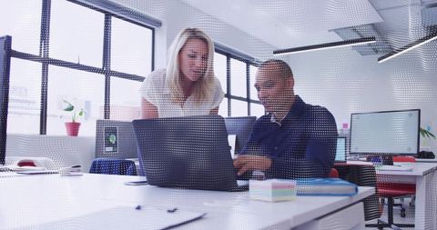 Two colleagues collaborating over laptop in bright modern open-plan office