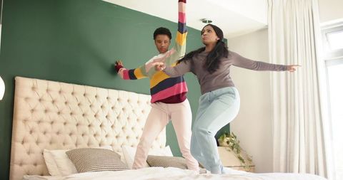 Friends joyfully jumping on bed in bright bedroom